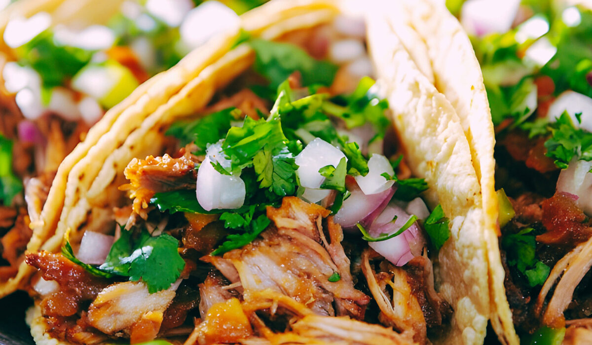 Three shredded beef tacos on a plate with veggie garnish
