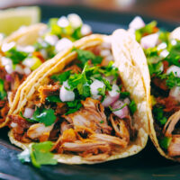 Three shredded beef tacos on a plate with veggie garnish
