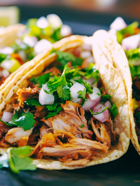 Three shredded beef tacos on a plate with veggie garnish
