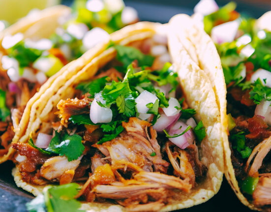 Three shredded beef tacos on a plate with veggie garnish