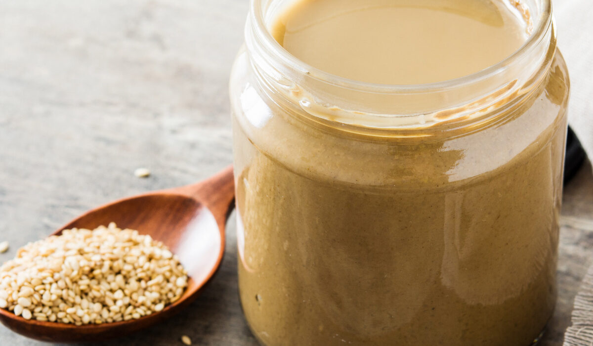 Tahini dressing in a glass jar with a spoon of sesame seeds next to it