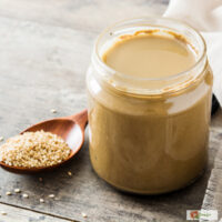 Tahini dressing in a glass jar with a spoon of sesame seeds next to it