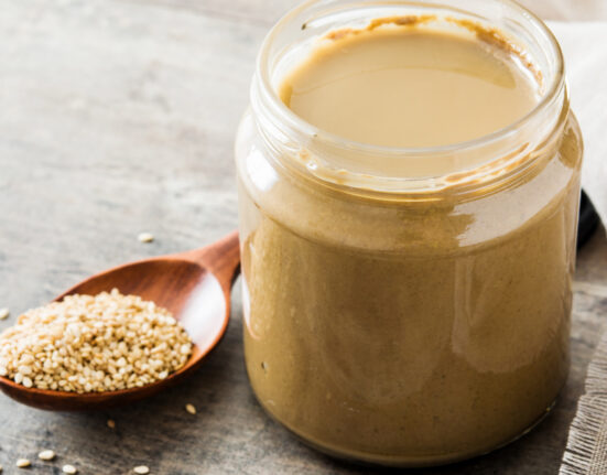 Tahini dressing in a glass jar with a spoon of sesame seeds next to it