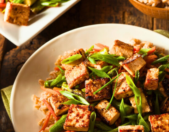 Tofu stir fry on a plate over rice with a serving dish of it next to the plate