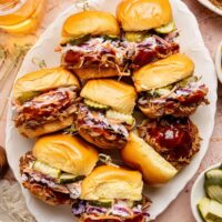 Overhead view of a platter of Pulled Pork Sliders topped with coleslaw and sliced pickles.