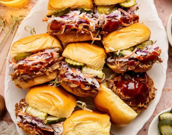Overhead view of a platter of Pulled Pork Sliders topped with coleslaw and sliced pickles.