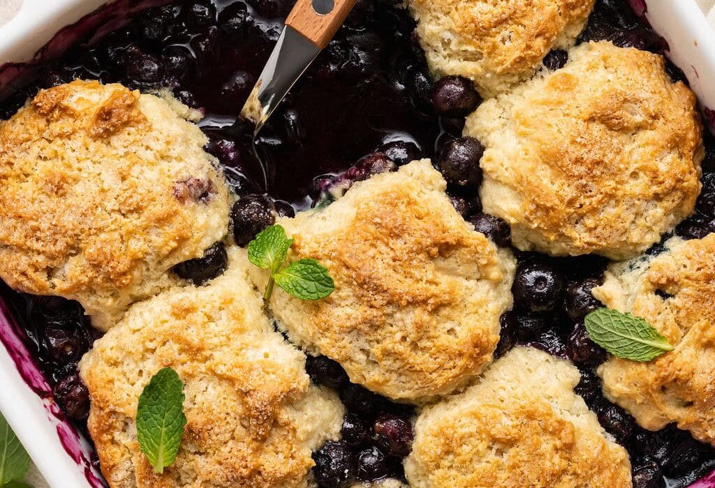 Overhead view of a baking dish filled with Blueberry Cobbler garnished with fresh mint leaves.