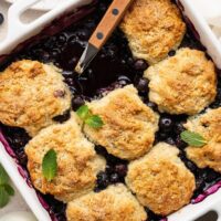 Overhead view of a baking dish filled with Blueberry Cobbler garnished with fresh mint leaves.