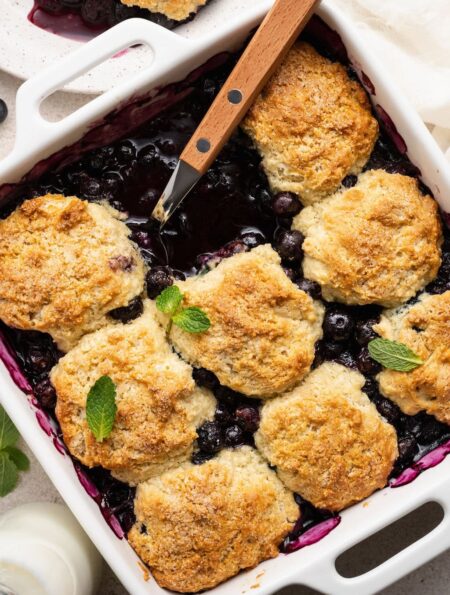 Overhead view of a baking dish filled with Blueberry Cobbler garnished with fresh mint leaves.