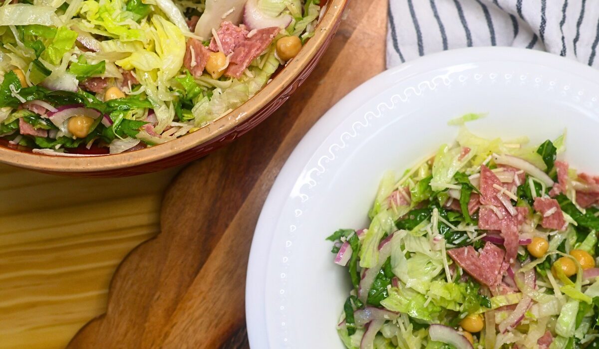 A bowl of la scala salad next to the mixing bowl of prepared salad