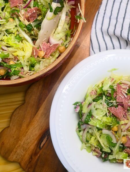 A bowl of la scala salad next to the mixing bowl of prepared salad