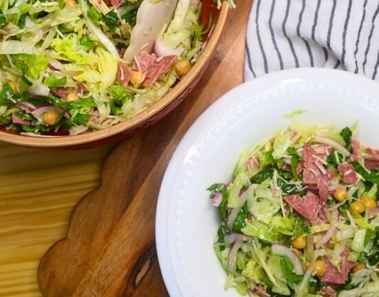 A bowl of la scala salad next to the mixing bowl of prepared salad