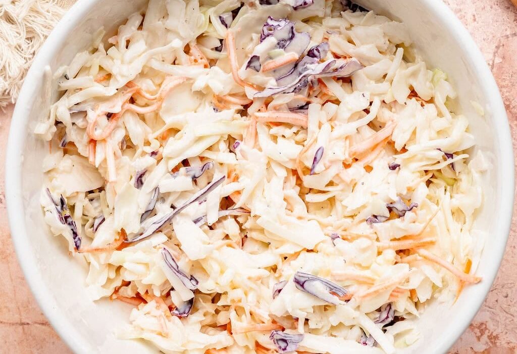 Overhead view of a white bowl filled with fresh coleslaw.