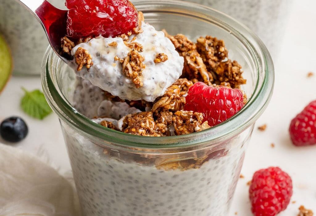 Close up view of a glass jar of chia pudding topped with raspberries and granola