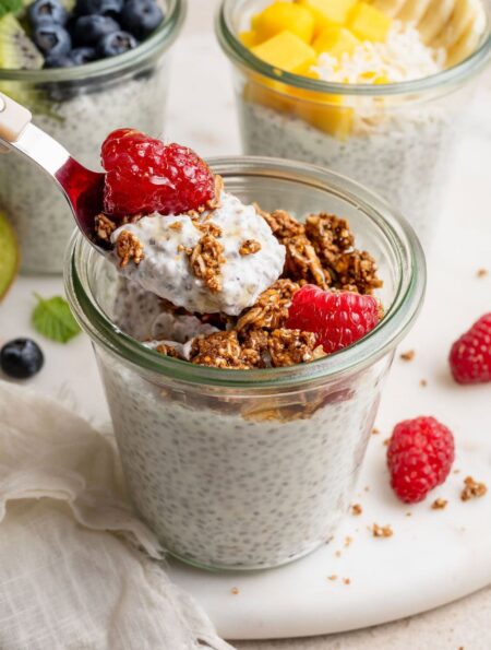 Close up view of a glass jar of chia pudding topped with raspberries and granola