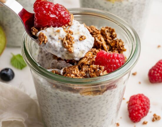 Close up view of a glass jar of chia pudding topped with raspberries and granola