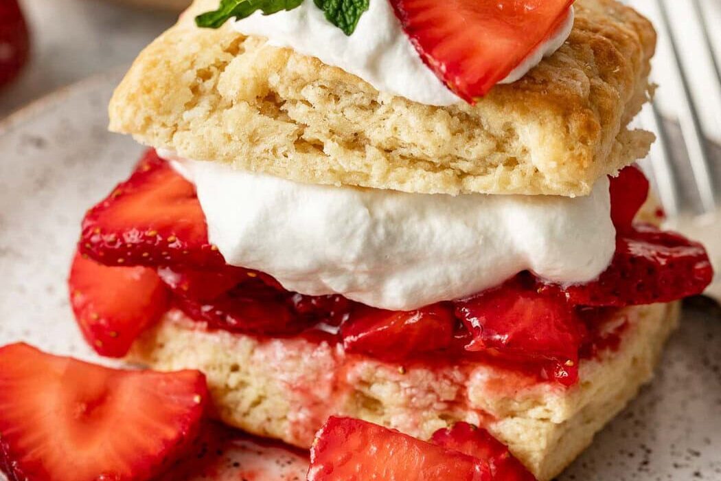 Close up view of a piece of Strawberry Shortcake showing the layers of biscuits, strawberries, whipped cream and garnish of fresh mint.