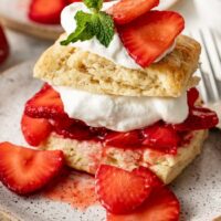 Close up view of a piece of Strawberry Shortcake showing the layers of biscuits, strawberries, whipped cream and garnish of fresh mint.