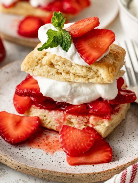 Close up view of a piece of Strawberry Shortcake showing the layers of biscuits, strawberries, whipped cream and garnish of fresh mint.