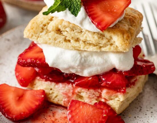 Close up view of a piece of Strawberry Shortcake showing the layers of biscuits, strawberries, whipped cream and garnish of fresh mint.