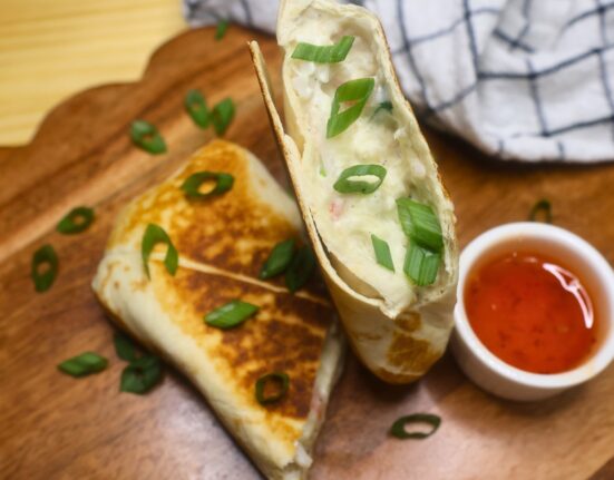 Overhead image of a crab rangoon burrito cut in half on a wooden serving tray with dipping sauce