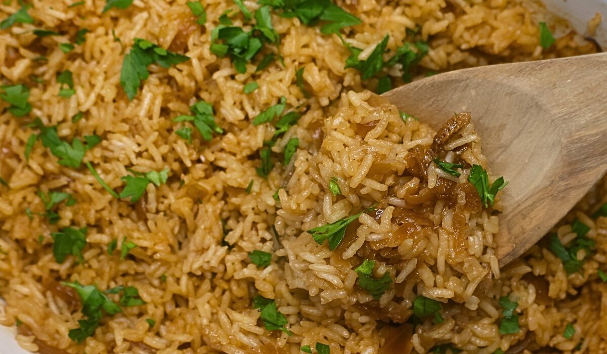 Stick of butter rice in a baking dish being served with a wooden spoon