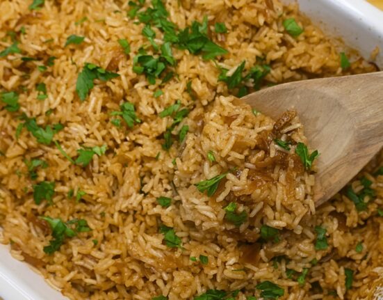 Stick of butter rice in a baking dish being served with a wooden spoon